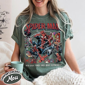 K&ouml;nnte beinhalten: Moosgr&uuml;nes T-Shirt mit einem Spider-Man-Motiv. Das Design zeigt die Worte "SPIDER-MAN" in Rot und Blau sowie Comic-Panels mit Spider-Man. Der Text "WITH GREAT POWER COMES GREAT RESPONSIBILITY" ist ebenfalls sichtbar.