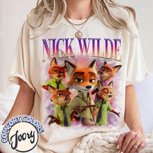 Puede incluir: Camiseta de color marfil con el personaje Nick Wilde de Zootopia. El gr&aacute;fico incluye el texto "NICK WILDE" en morado y naranja, junto con m&uacute;ltiples im&aacute;genes del personaje zorro. La camiseta tiene una etiqueta Comfort Colors.