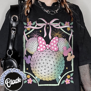May include: Black Comfort Colors t-shirt with a colourful graphic design. The design features two spherical shapes with a geometric pattern, a pink polka-dot bow, and floral and fireworks elements. The shirt has a distressed appearance.