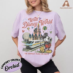 May include: Orchid-colored Comfort Colors t-shirt featuring a Walt Disney World graphic. The design includes a castle, monorail, Mickey Mouse, and the text "The Happiest Place on Earth."