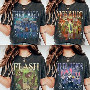 May include: Four dark gray t-shirts featuring characters from the animated movie Zootopia. Each shirt displays a different character or group of characters with their names: Chief Bogo, Nick Wilde, Flash, and Judy Hopps. The designs are in a vintage style.