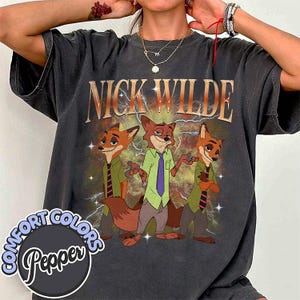 May include: Dark gray t-shirt featuring the text "NICK WILDE" above a cartoon image of three foxes. The foxes are wearing shirts and ties. The shirt has a distressed, vintage look with the words "COMFORT COLORS Pepper" in a circle at the bottom.