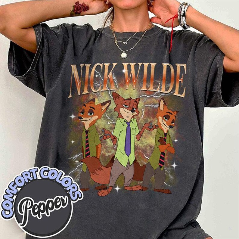 May include: Dark gray t-shirt featuring the text "NICK WILDE" above a cartoon image of three foxes. The foxes are wearing shirts and ties. The shirt has a distressed, vintage look with the words "COMFORT COLORS Pepper" in a circle at the bottom.