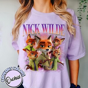 Puede incluir: Una camiseta de color lila claro con el texto "NICK WILDE" sobre un gr&aacute;fico del personaje Nick Wilde de la pel&iacute;cula Zootr&oacute;polis. El gr&aacute;fico incluye m&uacute;ltiples im&aacute;genes de Nick Wilde con camisa y corbata verdes.