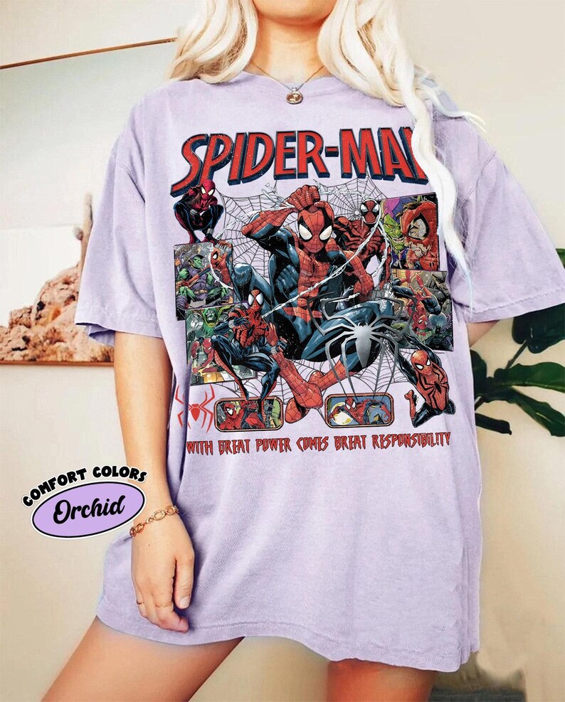 K&ouml;nnte beinhalten: Orchideenfarbenes T-Shirt mit einem Spider-Man-Motiv. Das Design enth&auml;lt die roten Worte "SPIDER-MAN" und verschiedene Spider-Man-Illustrationen. Der Text "WITH GREAT POWER COMES GREAT RESPONSIBILITY" ist ebenfalls sichtbar.