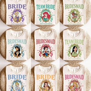Può includere: Nove magliette color crema con vari disegni di principesse. Le magliette presentano le parole "BRIDE", "TEAM BRIDE" e "BRIDESMAID" in diversi colori, insieme al testo "JUNE 2025" e "EMILY'S BACHELORETTE".