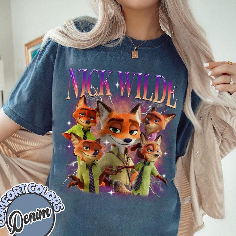 Puede incluir: Una camiseta azul marino con un gr&aacute;fico de Nick Wilde de la pel&iacute;cula Zootopia. El dise&ntilde;o incluye el texto "NICK WILDE" en una fuente p&uacute;rpura y rosa, con im&aacute;genes de Nick Wilde en varias poses. La camiseta tambi&eacute;n tiene el texto "COMFORT COLORS Denim" en un dise&ntilde;o circular.