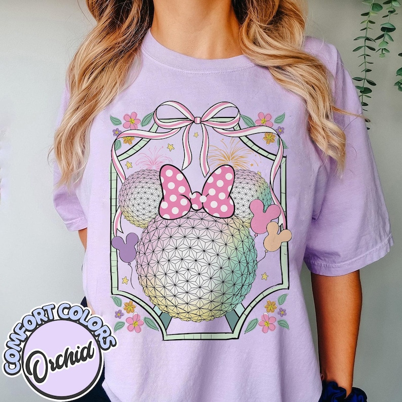 May include: A lilac Comfort Colors t-shirt with a graphic of a geometric sphere, a pink polka dot bow, Mickey Mouse ears, and floral details. The shirt has the words "Comfort Colors" and "Orchid" printed on it.
