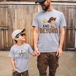 May include: Two gray t-shirts with cartoon character designs. One shirt features Woody with the text "AND BEYOND", and the other has Buzz Lightyear with "TO INFINITY". The shirts are worn by a father and child.