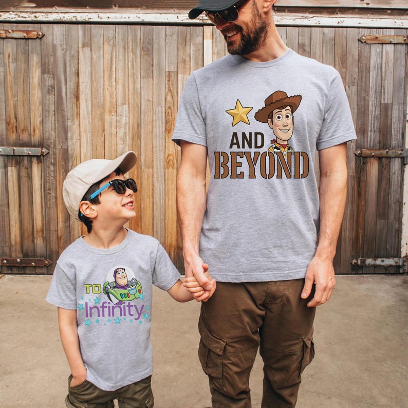 May include: Two gray t-shirts with cartoon character designs. One shirt features Woody with the text "AND BEYOND", and the other has Buzz Lightyear with "TO INFINITY". The shirts are worn by a father and child.