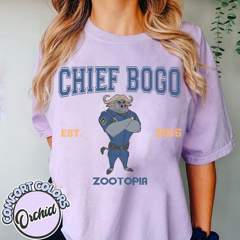 Puede incluir: Una camiseta de color lila claro con el texto "CHIEF BOGO" sobre una imagen de dibujos animados del Jefe Bogo de Zootopia. La camiseta tambi&eacute;n incluye el texto "EST. 2016" y "ZOOTOPIA". La camiseta es de Comfort Colors.