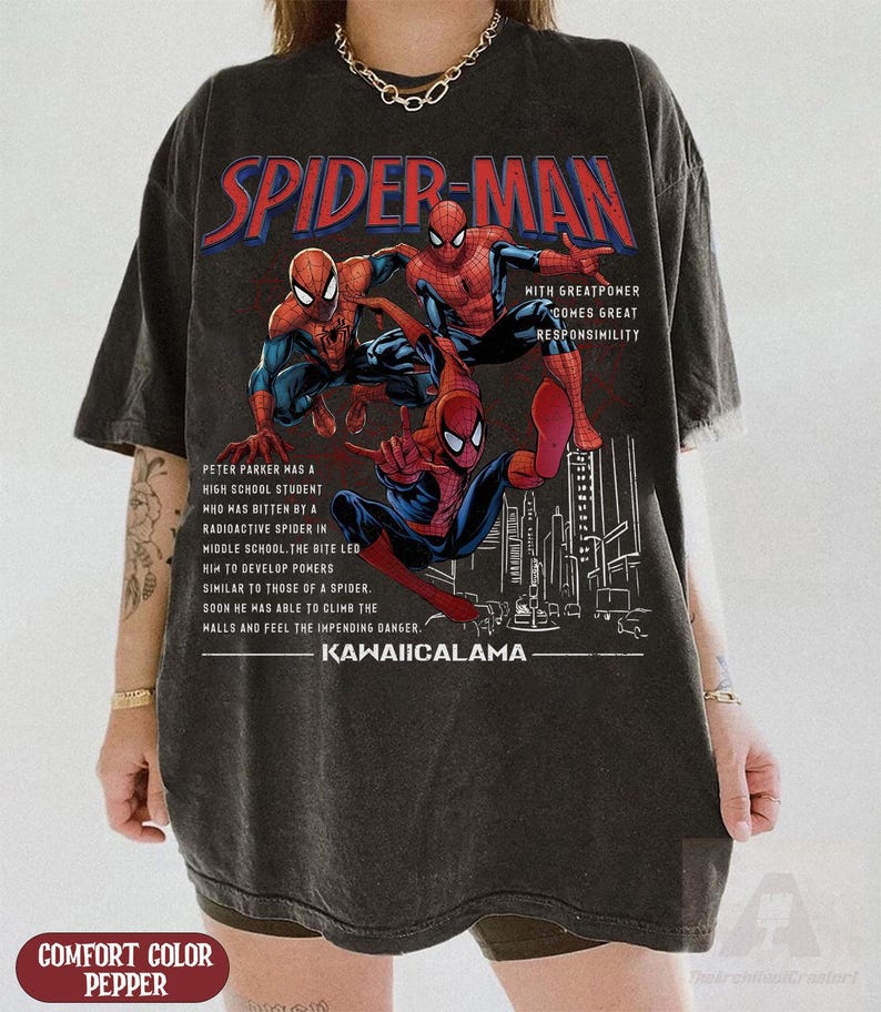 May include: Dark gray t-shirt featuring a graphic of Spider-Man in action poses. The design includes the text "SPIDER-MAN" in red and white, along with additional text describing the character's origin and the phrase "KAWAIICALAMA".