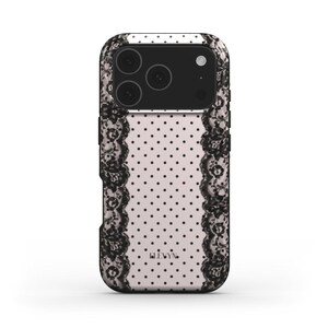 以下が含まれることがあります： 黒とピンクのレース模様の携帯電話ケース。ケースは、小さな黒い水玉模様のピンク色の背景が特徴です。黒いレースが側面を縁取っています。カメラ部分は黒です。ブランド名「LEVYN」が下部に印刷されています。