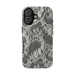 May include: A smartphone case with a white lace design on a dark grey backdrop. The case has a protective design, a camera aperture, and the brand name "ELEVVN" at the base. The case is designed to fit a smartphone.