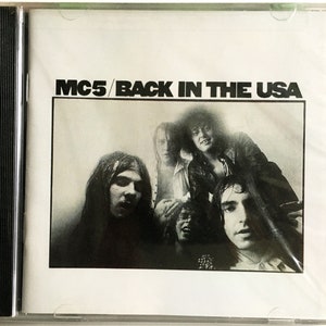 Könnte beinhalten: Ein Schwarzweißfoto einer Band, MC5, auf einem CD-Cover. Die Band steht vor einem weißen Hintergrund. Der Text "MC5/BACK IN THE USA" ist in Schwarz auf dem Cover gedruckt.