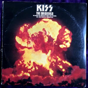 May include: Vintage vinyl record album cover for "KISS The Originals." The cover features the band's logo and album title in white text. The artwork depicts a fiery explosion with the band members' faces superimposed.