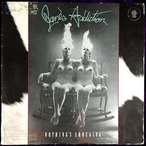May include: Album cover for Jane's Addiction's "Nothing's Shocking." The cover features two nude figures with flames atop their heads, seated in a rocking chair. The band's name is in neon green script above the figures.