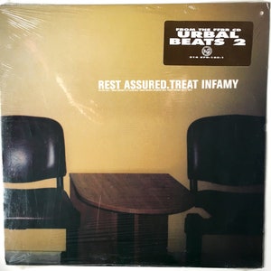 May include: A vinyl record cover with a yellow background and the text "REST ASSURED. TREAT INFAMY" in black. The cover features two black chairs and a brown table in front of a yellow wall. The top right corner of the cover has a sticker with the text "FROM THE FREE CD URBAL BEATS 2" in black and white.