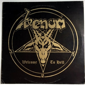 May include: A black vinyl record with a gold pentagram and a goat's head in the centre. The text "Venom" and "Welcome To Hell" are written in gold lettering.