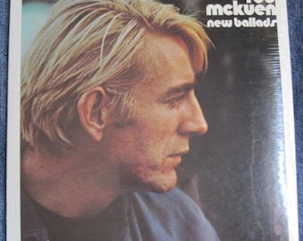 May include: A vintage vinyl record album cover featuring a close-up portrait of Rod McKuen. The album title "New Ballads" is printed in white letters on a black background.