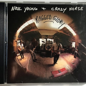 May include: A CD case with a photo of Neil Young and Crazy Horse in a recording studio. The text "Neil Young + Crazy Horse Ragged Glory" is written on the front of the case.