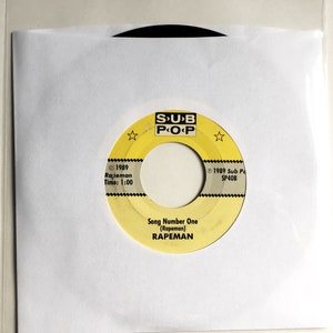 May include: A yellow vinyl record with black text that reads "SUB POP" and "Song Number One (Rapeman) RAPEMAN". The record label also includes the copyright information "© 1989 Rapeman Time: 1:00" and "© 1989 Sub Pa SP40B".