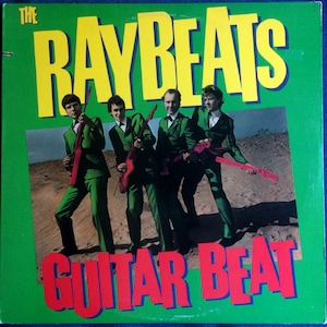 May include: A vintage vinyl record cover featuring a band called "The Raybeats" with the title "Guitar Beat". The cover features a photo of four men in green suits holding guitars, standing in a desert landscape.