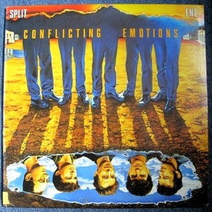 Puede incluir: Una portada de álbum de vinilo vintage con la banda ENZ. El título del álbum es "Split Ends" y la portada del álbum presenta a un grupo de hombres de pie en una línea con sus reflejos en un charco de agua debajo.