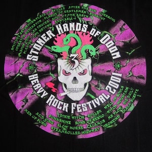May include: Black t-shirt with a circular graphic of a skull with snakes coming out of its head. The graphic is surrounded by a purple and green tie-dye pattern and the text "Stoner Hands of Doom Heavy Rock Festival 2001". The text lists the names of bands including "Dixie Witch", "Sons of Cerro", "Witch Mountain", and "Mr. Plow".