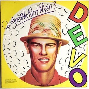 May include: A yellow, green, red, and purple album cover with the word "DEVO" in large letters. The cover features a man wearing a straw hat with a green, white, and yellow pattern. The text "Are We Not Men?" is written in purple on the top left corner of the cover.