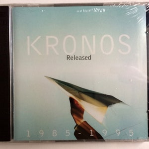 May include: A CD case with a blue background and a white paper airplane flying out of a hand. The text "KRONOS" is in white letters at the top of the case. The text "Released" is in white letters below the band name. The text "1985-1995" is in white letters at the bottom of the case.