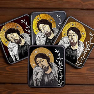 May include: Set of five embroidered patches featuring a religious icon with a gold halo, brown hair, and a beard, embracing a lamb. The patches have a square shape with a dark border and are set against a wooden background.