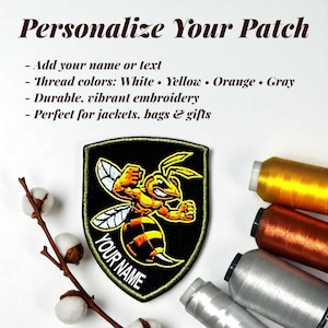 May include: Embroidered patch featuring a cartoon wasp in yellow and orange on a black background. The patch has the text "YOUR NAME" and "Personalize Your Patch". The image also shows spools of thread in various colours.