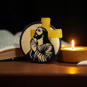 Może przedstawiać: Haftowana naszywka przedstawiająca Jezusa ze złotym krzyżem. Obraz przedstawia Jezusa ze złożonymi dłońmi w modlitwie, na beżowym tle. W tle zapalona świeca i otwarta książka.