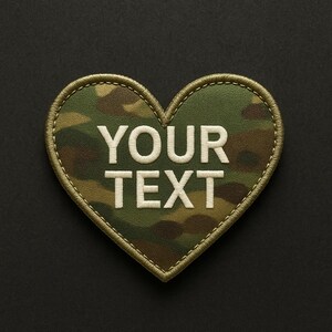 Puede incluir: Parche en forma de corazón con un patrón de camuflaje en tonos verdes, marrones y beige. El parche presenta el texto bordado "YOUR TEXT" en blanco, con un borde verde claro y cosido con hilo a juego.