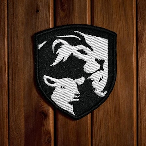 May include: Black and white embroidered patch in a shield shape. The patch design features a lamb, a lion, and a bird. The patch is suitable for a jacket, backpack, or other clothing items.