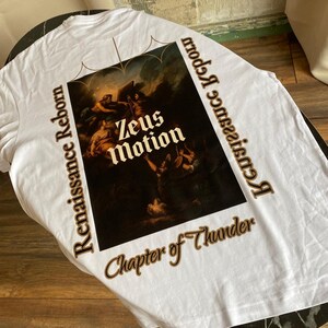 May include: White t-shirt featuring a Renaissance-style painting with the text "Zeus Motion" and "Renaissance Reborn" in brown. The shirt also includes the phrase "Chapter of Thunder". The shirt is made of a soft material.