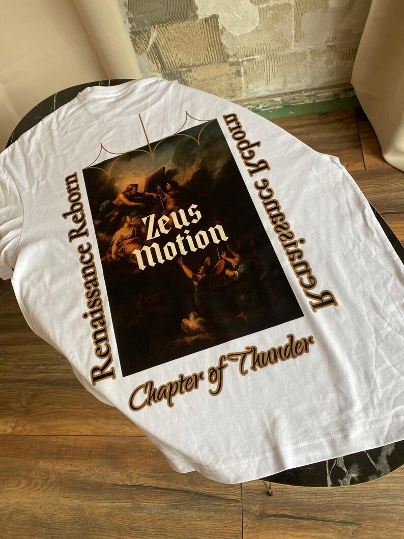 May include: White t-shirt featuring a Renaissance-style painting with the text "Zeus Motion" and "Renaissance Reborn" in brown. The shirt also includes the phrase "Chapter of Thunder". The shirt is made of a soft material.