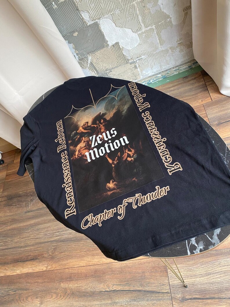 May include: Black long-sleeve shirt featuring a Renaissance-style painting with the text "Zeus Motion" in white. The shirt also has the text "Renaissance Reborn" and "Chapter of Thunder" in a gold color.