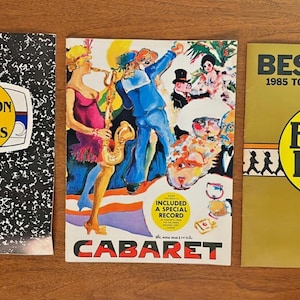 Puede incluir: Tres carteles de teatro vintage. El primero es una portada de cuaderno con "Brighton Beach Memoirs" en un círculo amarillo. El segundo es un colorido cartel de "Cabaret". El tercero es un cartel de "Biloxi Blues", ganador del premio Tony de 1985.