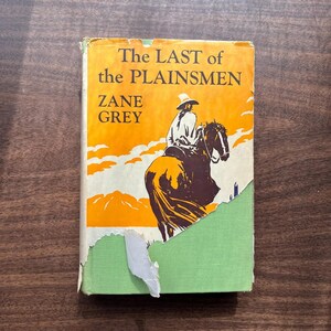 May include: Vintage book cover of "The Last of the Plainsmen" by Zane Grey. The cover features an illustration of a cowboy on horseback against an orange and yellow background. The book has a green spine and shows signs of wear.