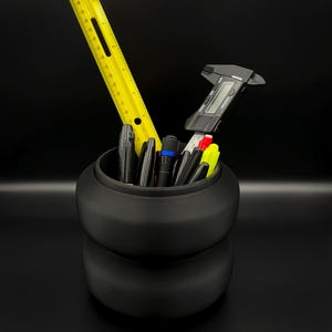 May include: A black, two-tiered desk organizer holding various office supplies. A yellow ruler and a digital caliper stand out among the pens and markers. The organizer is set against a black background.