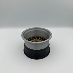 May include: A three-tone car wheel rim. The rim is composed of a gold-colored center, a gray mid-section, and a black base. The wheel has a multi-spoke design.