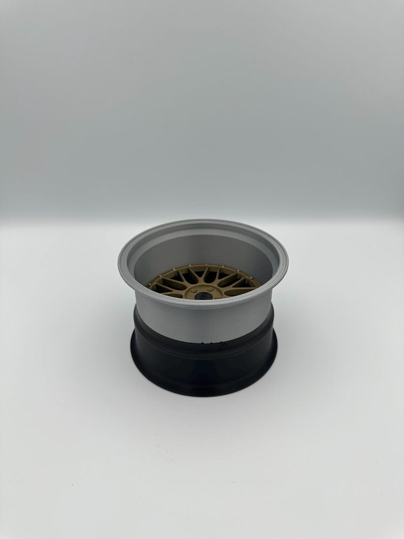 May include: A three-tone car wheel rim. The rim is composed of a gold-colored center, a gray mid-section, and a black base. The wheel has a multi-spoke design.