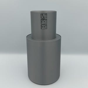 May include: A gray cylindrical object with the letters "HKS" embossed on the top section. The object has a two-tiered design, with a smaller cylinder stacked on a larger one. The background is plain white.