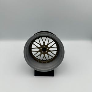 May include: A gray and bronze alloy wheel with a multi-spoke design. The wheel is displayed on a black stand against a white background. The wheel's rim is gray, and the spokes are bronze.