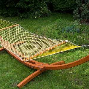 Könnte beinhalten: Ein Holz-Hängemattenständer mit einer gelben und weißen Seilhängematte. Der Ständer ist aus Naturholz gefertigt und hat ein geschwungenes Design. Die Hängematte hängt am Ständer und ist einsatzbereit.