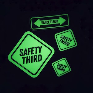 May include: Four neon green stickers with black text on a black background. The stickers include the phrases "DANCE FLOOR" with arrows, and "SAFETY THIRD". One sticker has the website address "WWW.HECKA.FUN".
