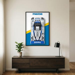 Puede incluir: Un póster de pared rectangular vertical que muestra una vista cenital de un coche de carreras Mazda blanco y azul con el número 18. El fondo es blanco con una franja diagonal amarilla y azul. El logotipo de Mazda aparece impreso arriba y abajo.