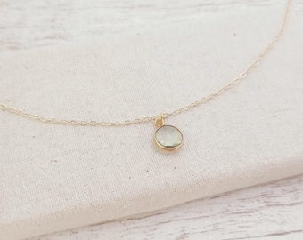 May include: A delicate gold chain necklace with a small, round, light green gemstone pendant.